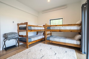 Ein Zimmer mit zwei Etagenbetten, einem kleinen Tisch mit Decke, einem Fenster mit Blick auf Bäume und einem weißen Teppich.