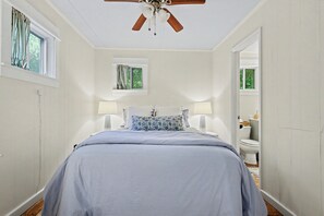 A bedroom with a bed, two bedside lamps, a ceiling fan, and a window with curtains.