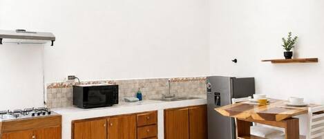 Een praktische keuken met houten kastjes, een ingebouwde magnetron, een koelkast en een kleine eettafel met stoelen.