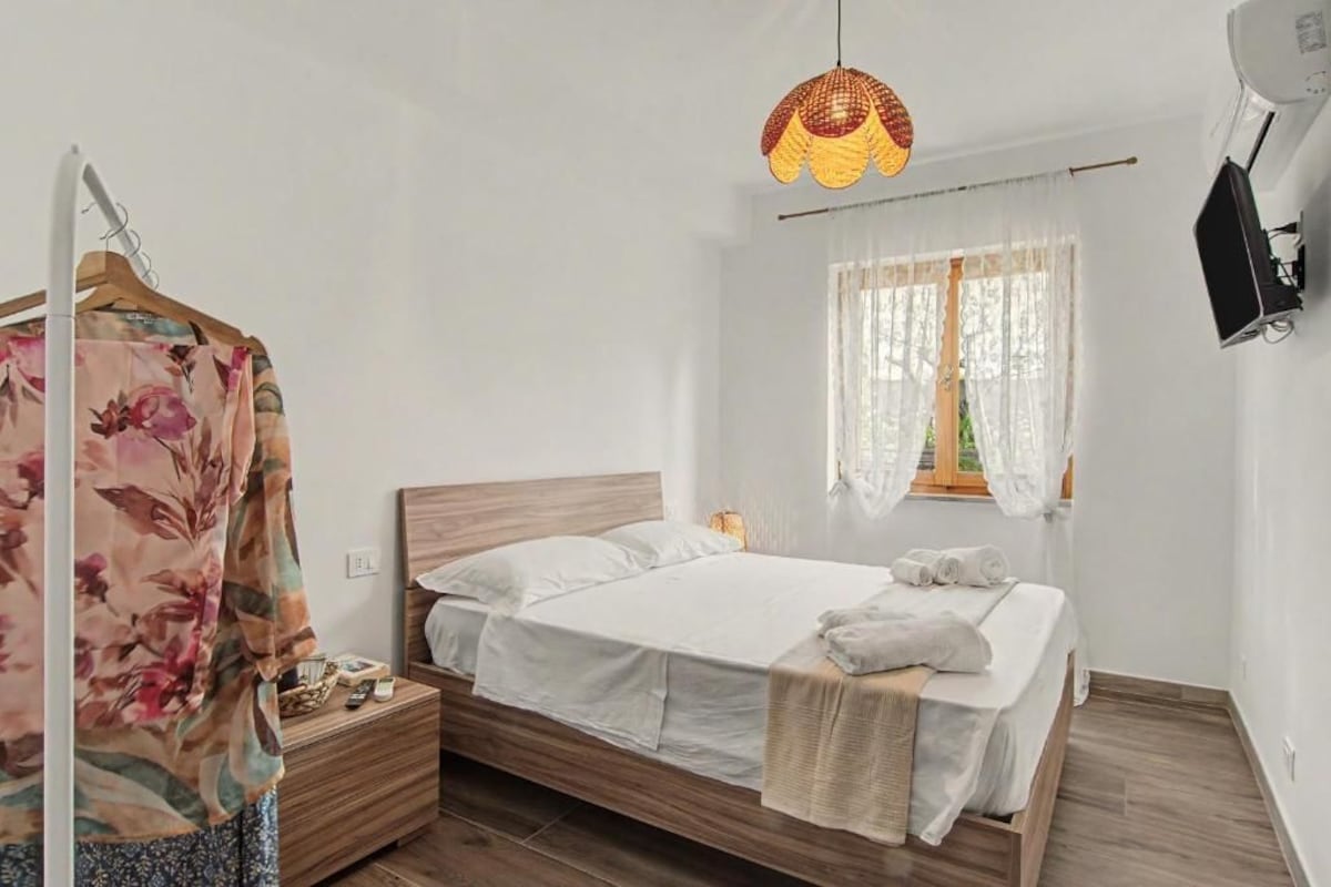 A bedroom with a bed, bedside table, lamp, and a window with curtains.