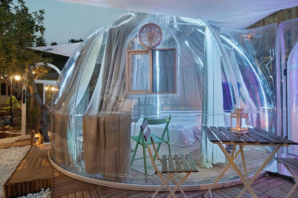 A transparent dome structure with a table and chairs inside, surrounded by a wooden deck.