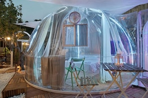 A transparent dome structure with a table and chairs inside, surrounded by a wooden deck. - Domus Olea Ecobio house (Oliveto Citra)