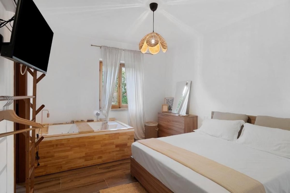 A bedroom with a wooden bed, a bedside table, a mirror, a hanging light fixture, and a window with curtains.