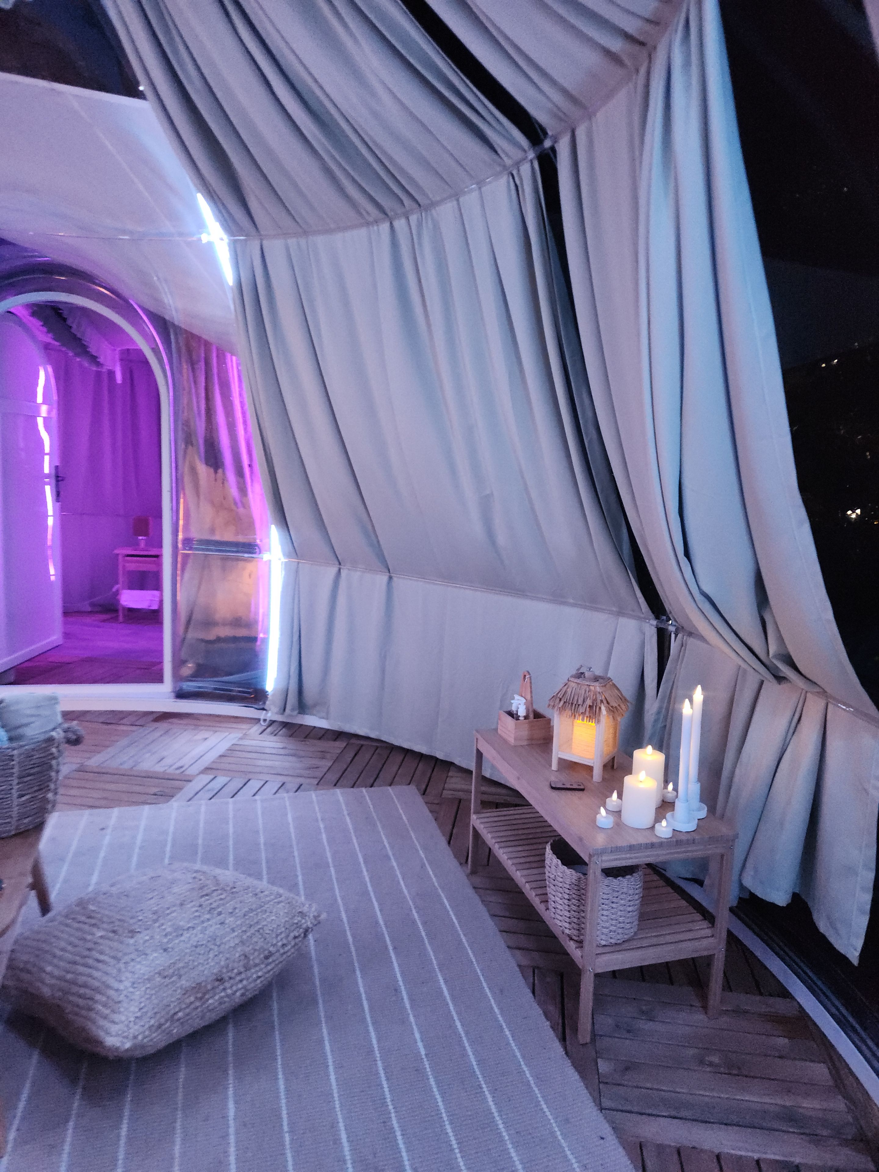 A tented area with a wooden bench, cushions, a small table with candles, and a lantern.