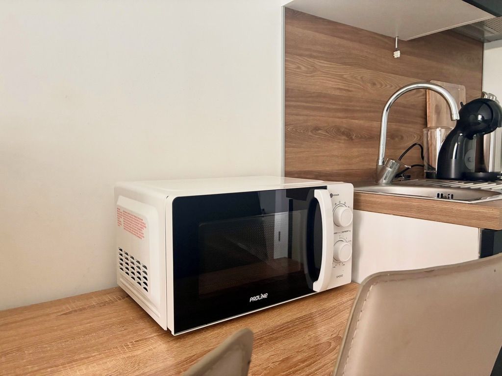 Un four à micro-ondes compact doté d’un écran numérique, placé sur un plan de travail en bois, à côté d’un évier avec un robinet.