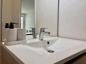 Un lavandino da bagno bianco con rubinetto cromato, uno specchio sopra e un piccolo contenitore con articoli da toilette a sinistra.