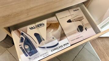 Un tiroir contenant un fer à vapeur à semelle en céramique, un sèche-cheveux puissant de la marque BaBytiss et un fer sans fil de la même marque.