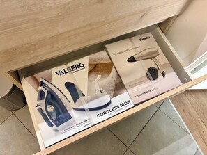 Un cassetto contenente un ferro da stiro a vapore con base in ceramica, un asciugacapelli liscio BaBytiss e un ferro da stiro BaBytiss senza fili.