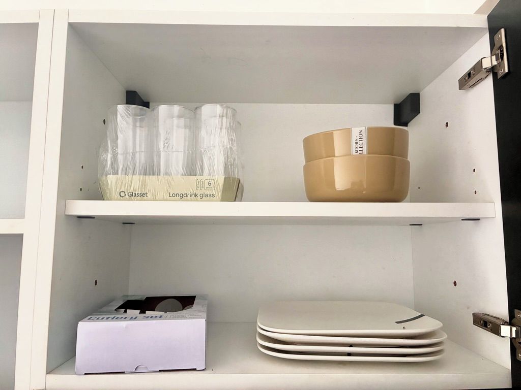 Un meuble blanc avec des étagères contenant de la verrerie, une boîte et des assiettes empilées.