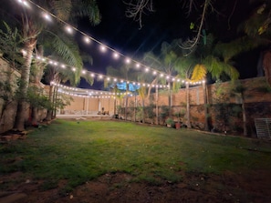 Un espacio exterior con pared de ladrillo, palmeras y luces colgantes.
