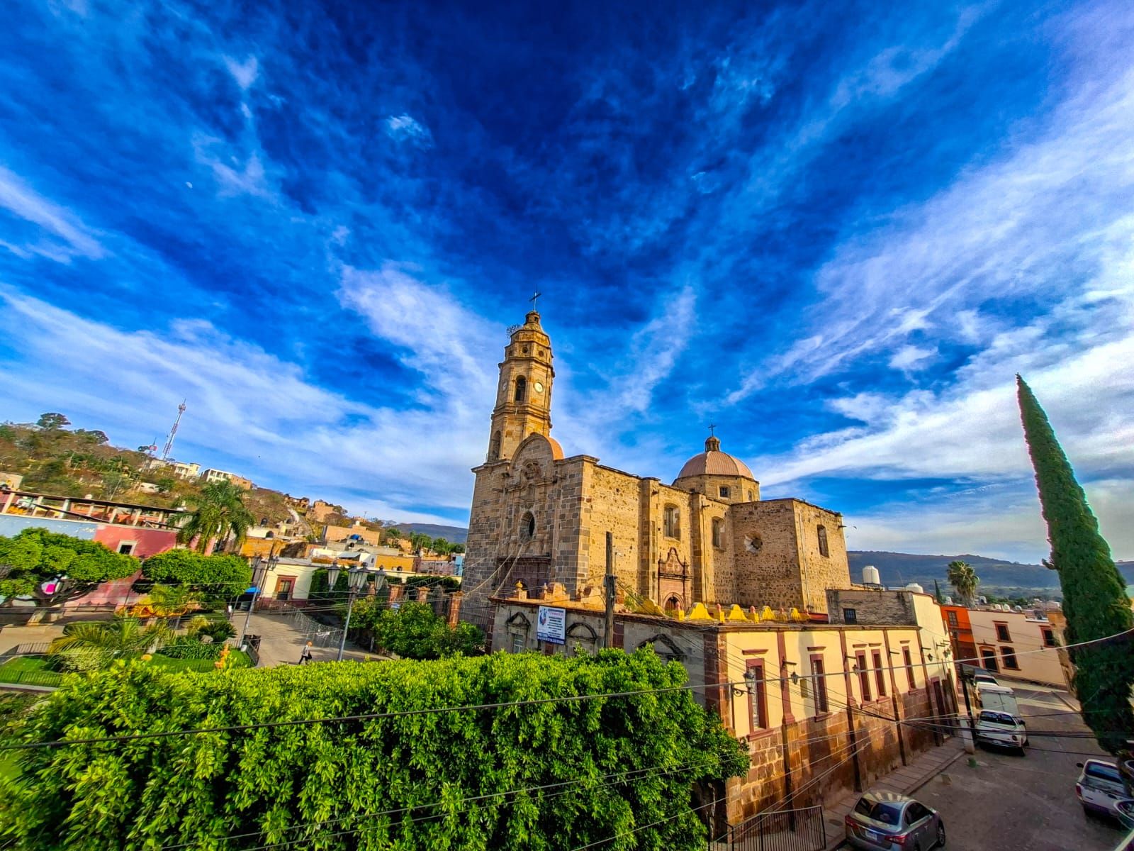 Una iglesia histórica con un campanario destacado, rodeada de edificios residenciales y follaje.
