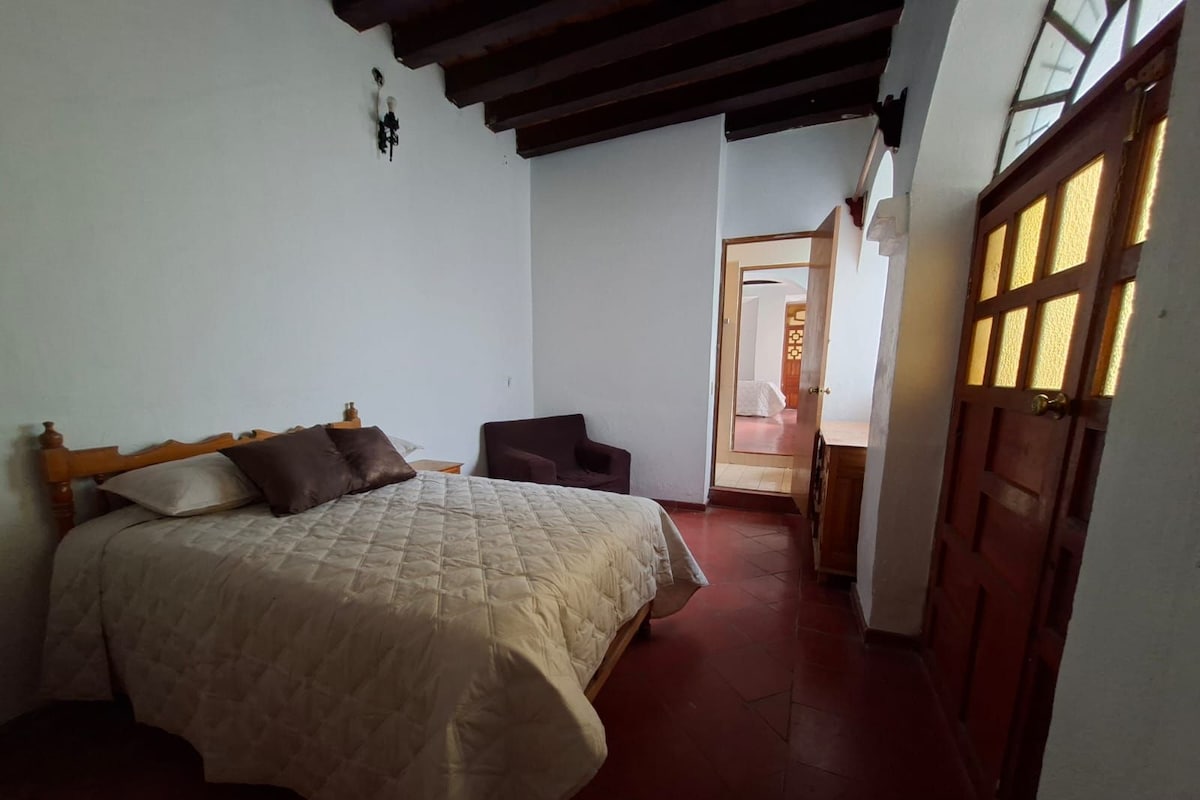 A bedroom with a bed, a chair, and a door leading to another room.