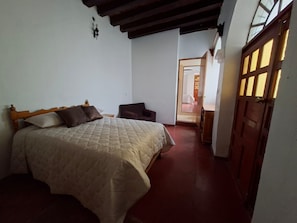 A bedroom with a bed, a chair, and a door leading to another room. - casona arcana  (Cuquío)