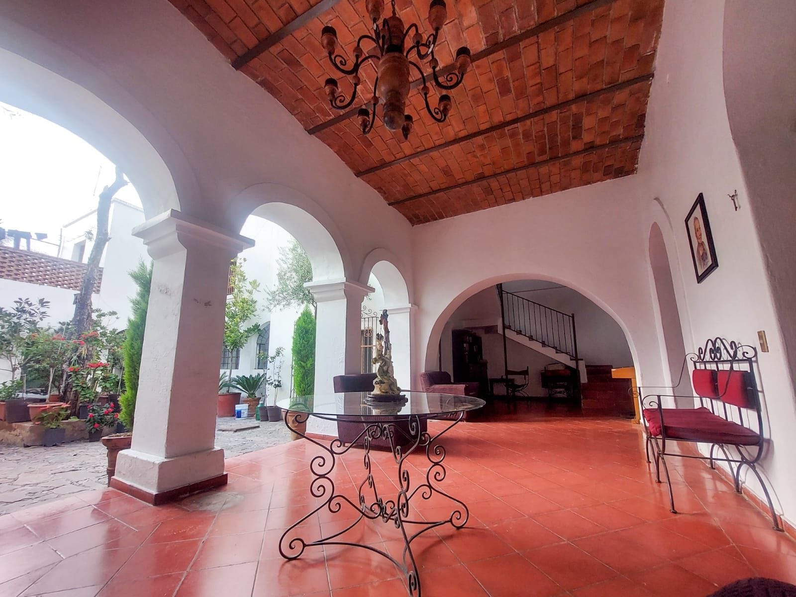 An interior courtyard with arches, a central table, and a staircase leading to an upper level.