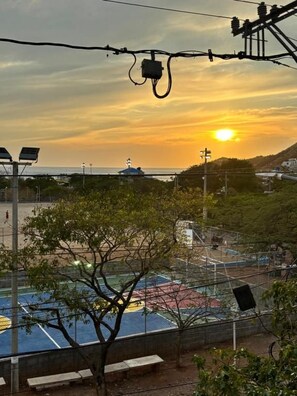 A sports court with a bench, a tree, and a sunset in the background.