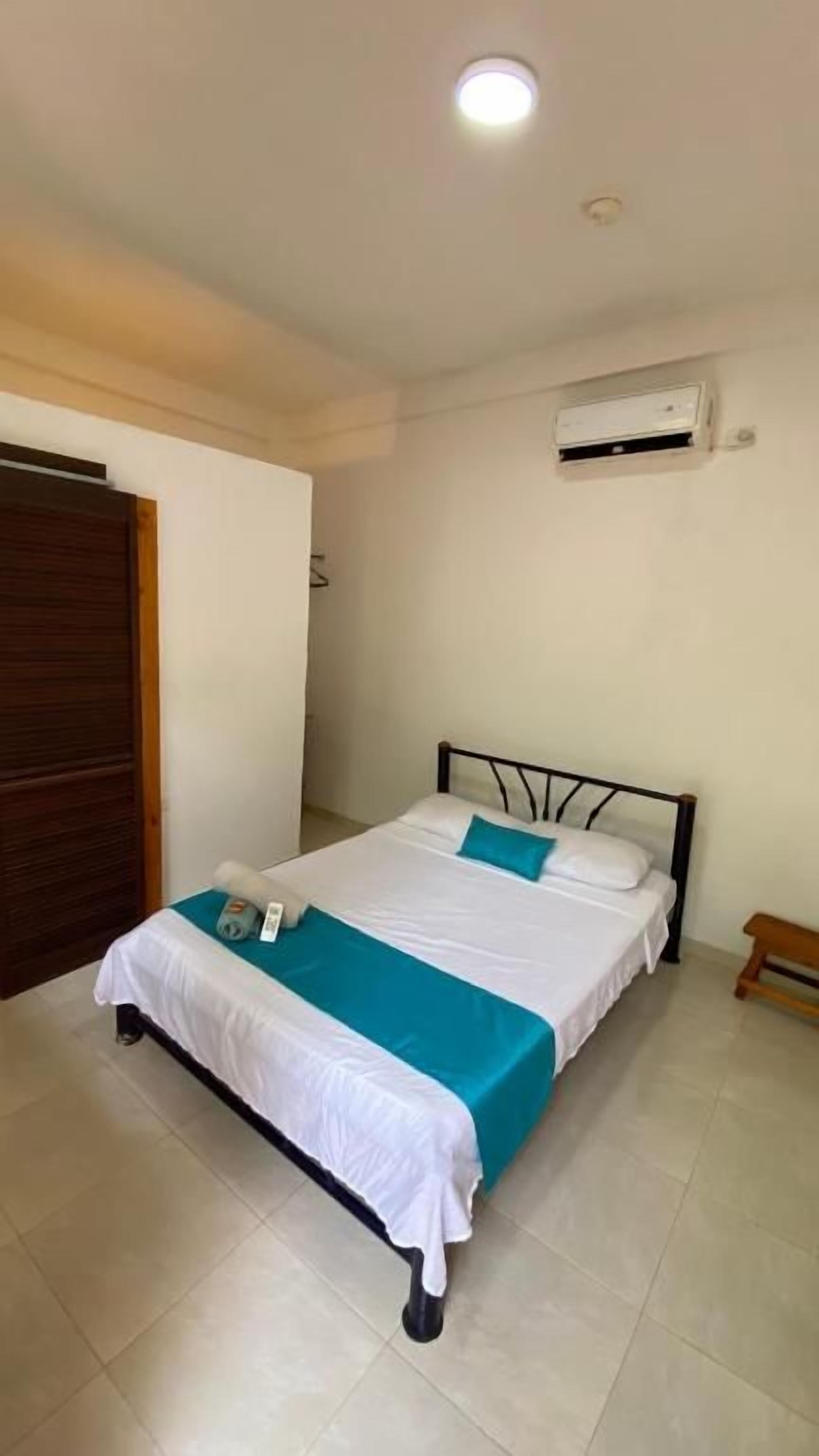 A single bed with a white and blue bedspread, a bedside table, and an air conditioning unit on the wall.