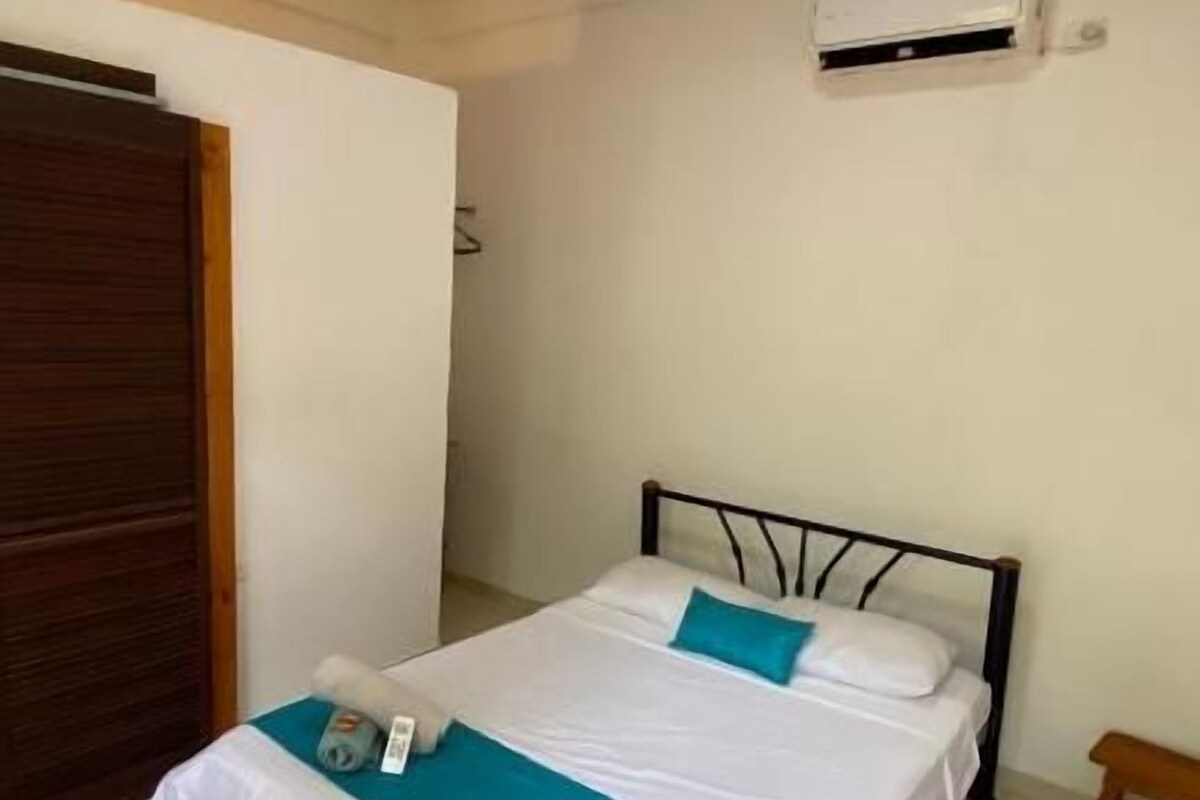 A single bed with a white and blue bedspread, a bedside table, and an air conditioning unit on the wall.
