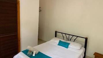 A single bed with a white and blue bedspread, a bedside table, and an air conditioning unit on the wall.
