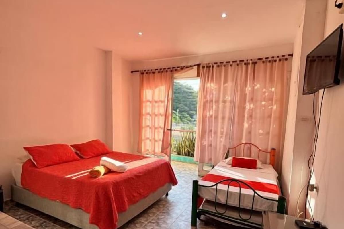 A hotel room with two beds, a TV, and a view of greenery outside.