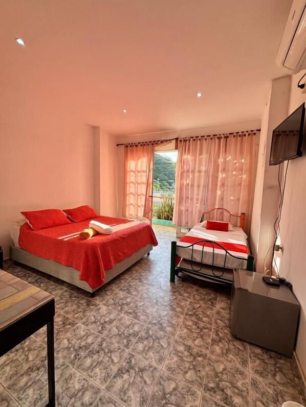 A hotel room with two beds, a TV, and a view of greenery outside.