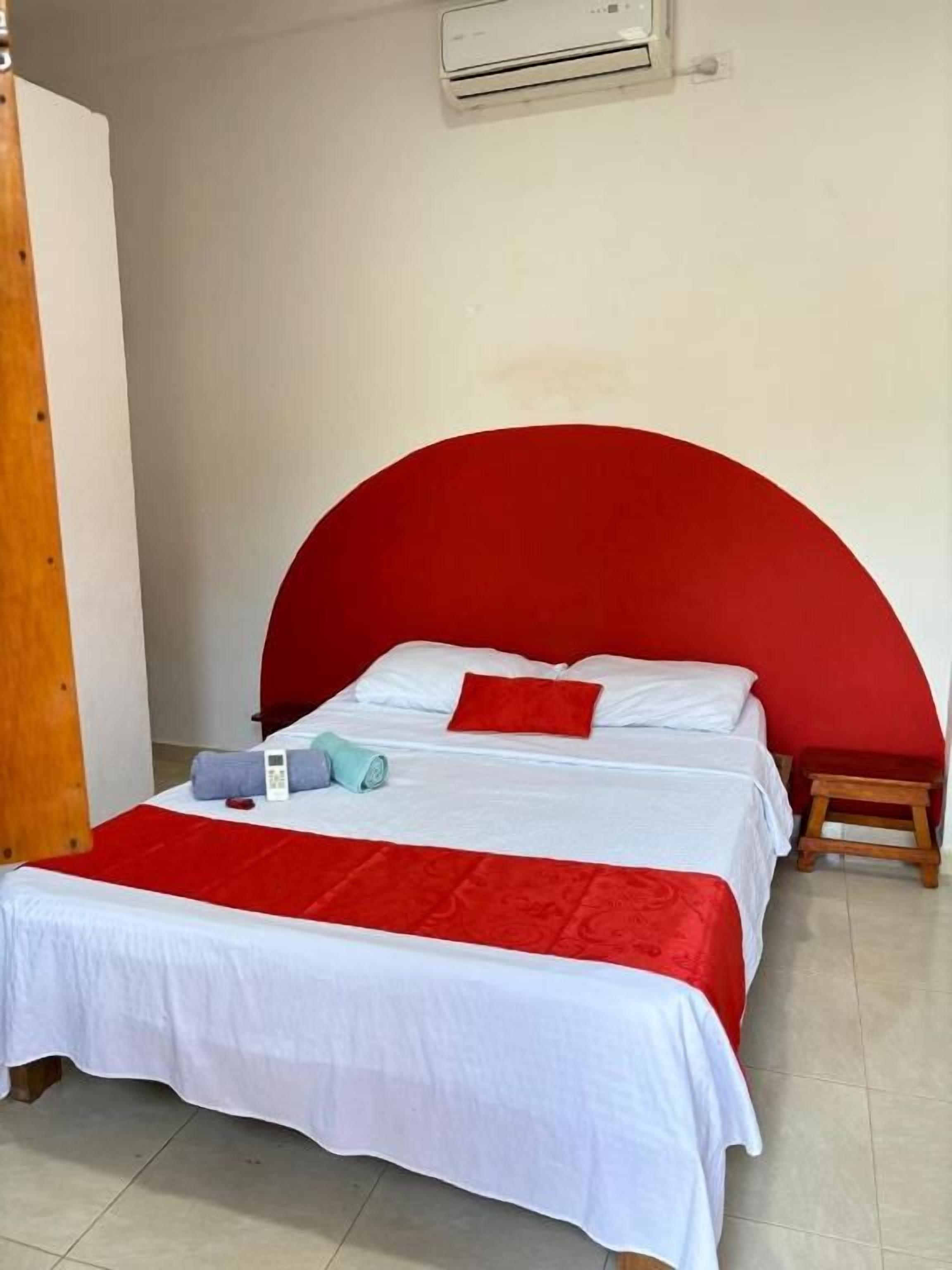 A single bed with a red headboard, white bedding, and a small wooden stool beside it.