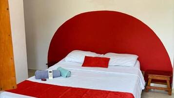 A single bed with a red headboard, white bedding, and a small wooden stool beside it.