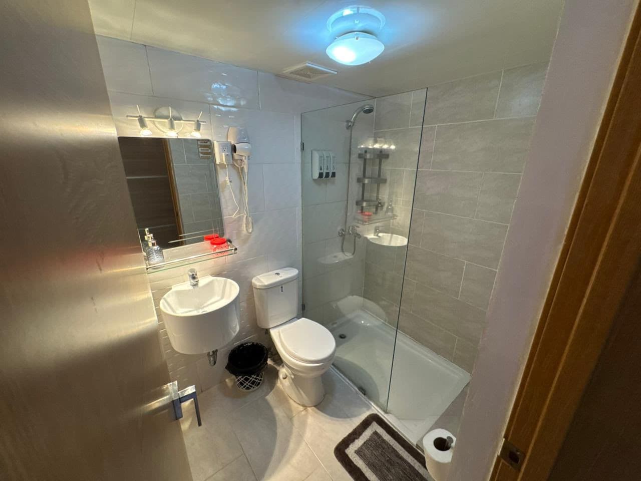 Ein modernes Badezimmer mit Duschkabine aus Glas, Toilette in Weiß und Waschbecken mit Spiegel darüber.