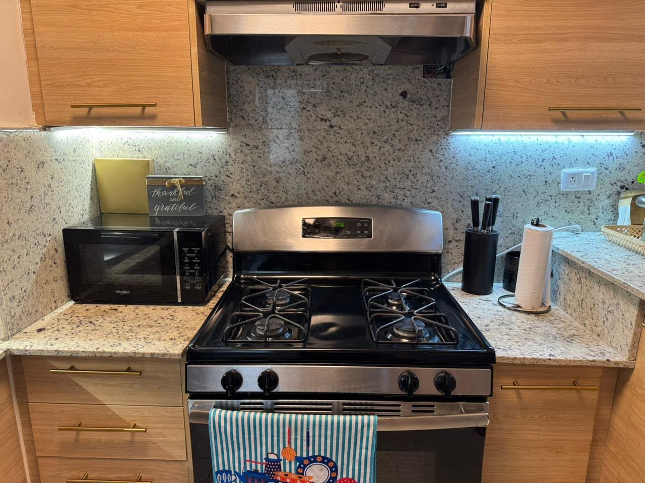 Een keuken met een magnetron, fornuis en houten keukenkastjes.