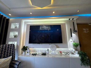 Ein modernes Wohnzimmer mit einem an der Wand befestigten Flachbildfernseher, einer weißen Unterhaltungsanlage darunter und einem gemusterten Sessel.