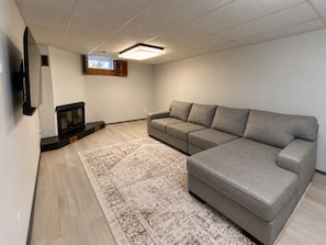 Una sala de estar con un sofá modular, un televisor de pantalla plana montado en la pared, una chimenea y una alfombra estampada.