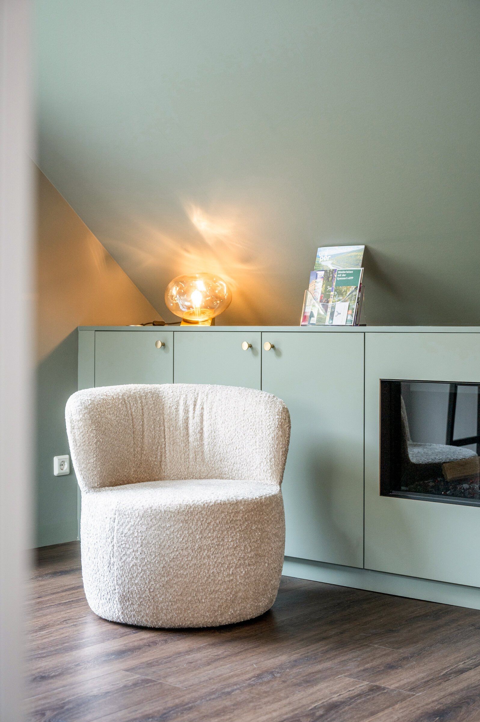 A room with a round, textured chair, a cabinet with a globe lamp, and a framed item on top.