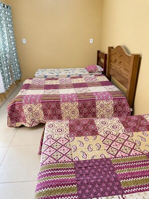 Ein Zimmer mit zwei Betten, jeweils mit einem gemusterten Bettbezug, einem Holz-Kopfteil und einem Vorhang mit Blattmuster.