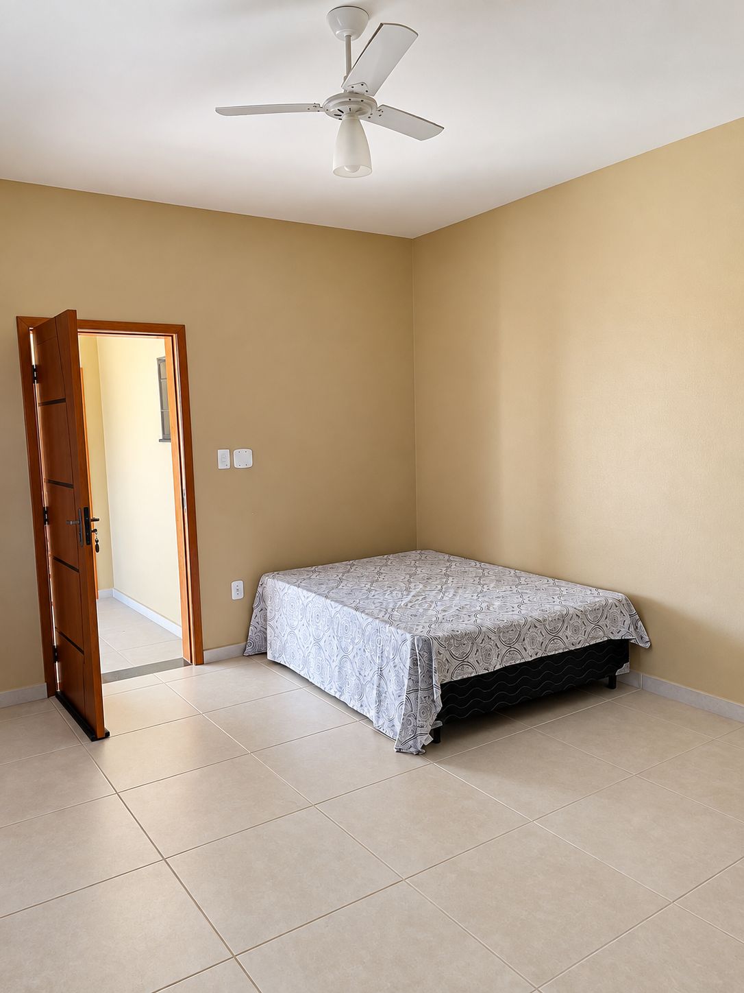 A bedroom with a bed, a ceiling fan, a door, and a light switch.
