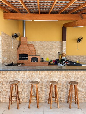 Eine Küche mit Backofen aus Ziegeln, Holzstühlen und einer gefliesten Spritzschutzwand.