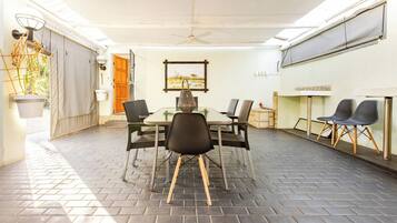 Una habitación con piso de ladrillo, una mesa con sillas, un ventilador de techo y un cuadro colgado en la pared.