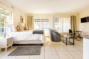 Habitació d'hotel amb un llit, escriptori, cadira, televisió i finestres grans.