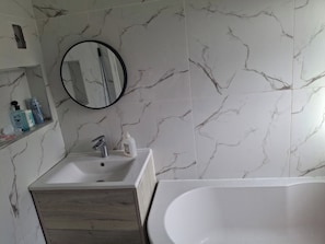 A bathroom with a marble wall, a sink with a mirror, and a bathtub. - House Sleeps 5 With Wifi (Ilford)