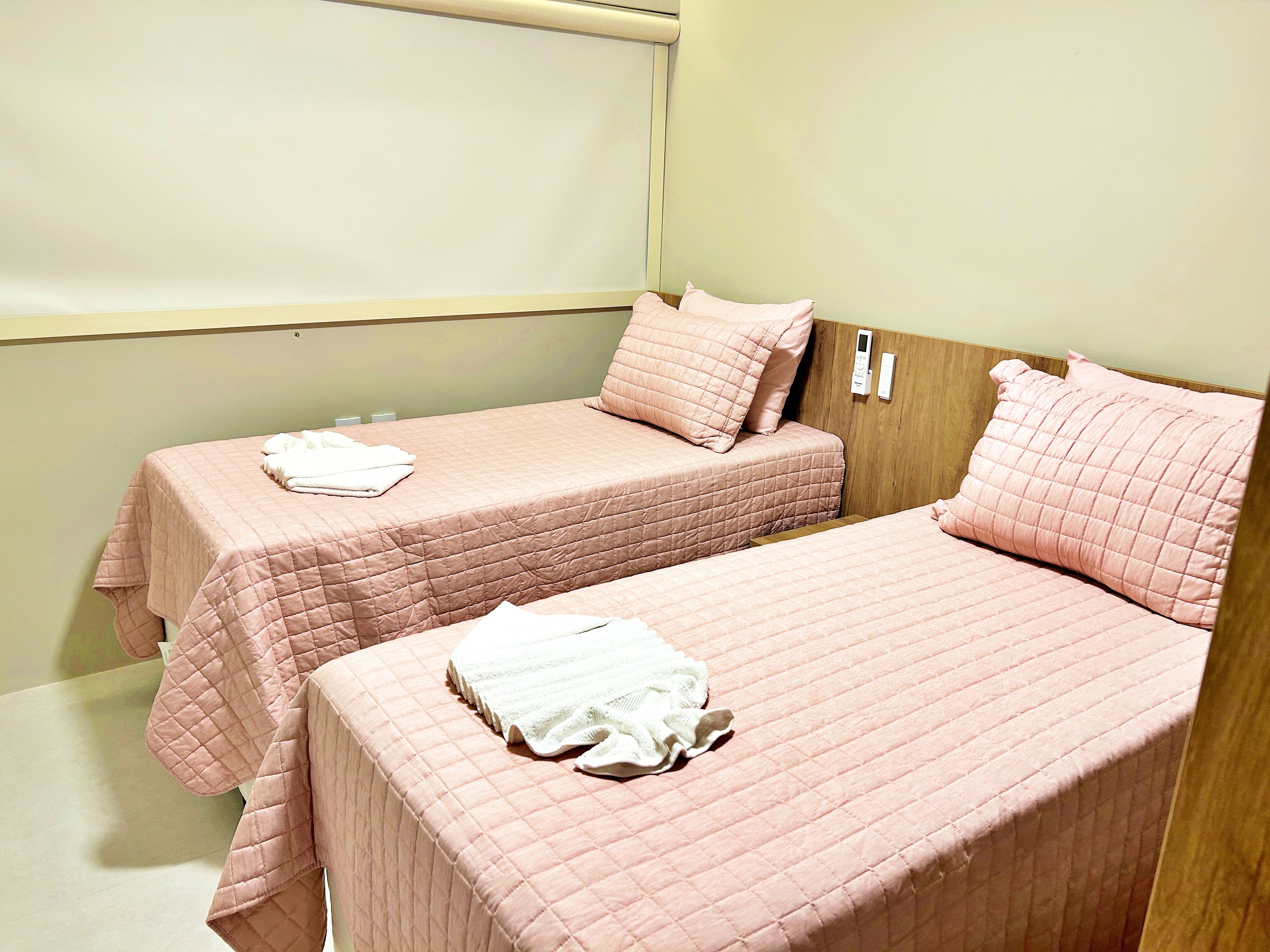 A room with two beds, each with a pink quilted bedspread and pillows, and a white towel on each bed.