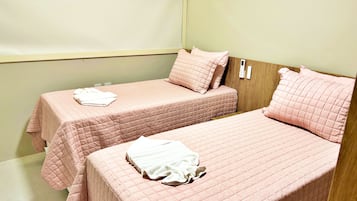 A room with two beds, each with a pink quilted bedspread and pillows, and a white towel on each bed.