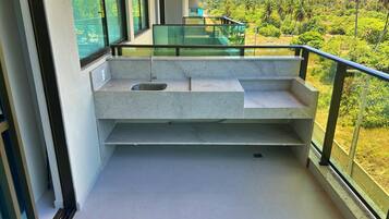 A modern balcony with a built-in sink and a glass railing overlooking a lush landscape.