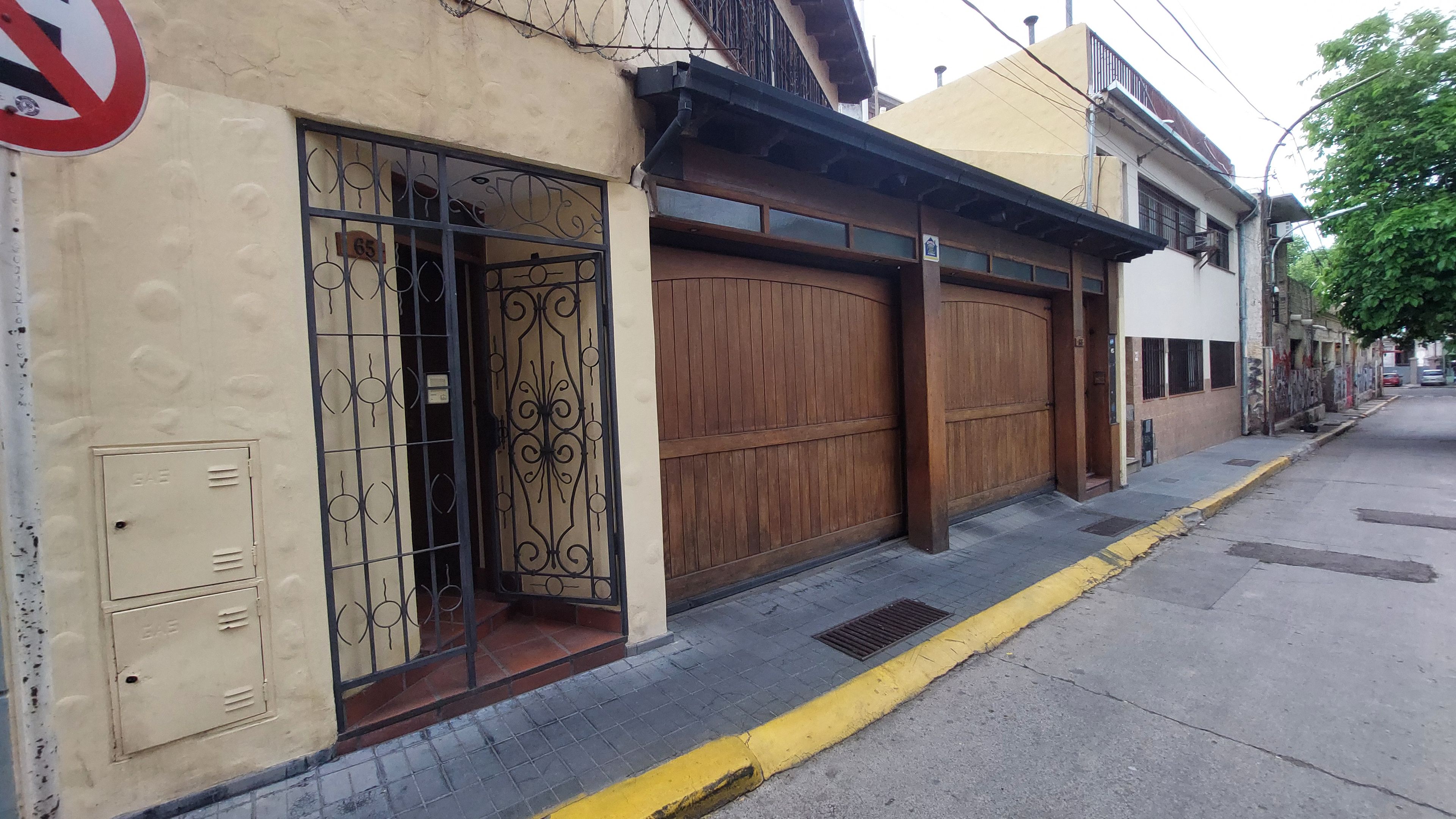 Vista de la calle con un edificio que tiene una puerta de garaje de madera grande, un portón de metal y una borda amarilla.