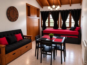 Ein Zimmer mit einer Couch, einem Tisch mit Stühlen, einem Bett, einem Holzschrank und einer Wanduhr.