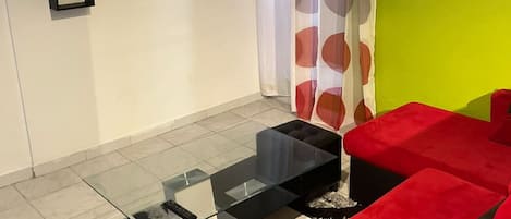 A living room with a flat-screen TV, red sofas, a glass coffee table, and a patterned rug.