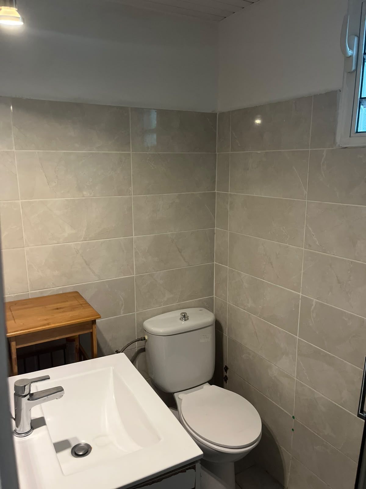 A small bathroom with a white sink, toilet, and a wooden stool.