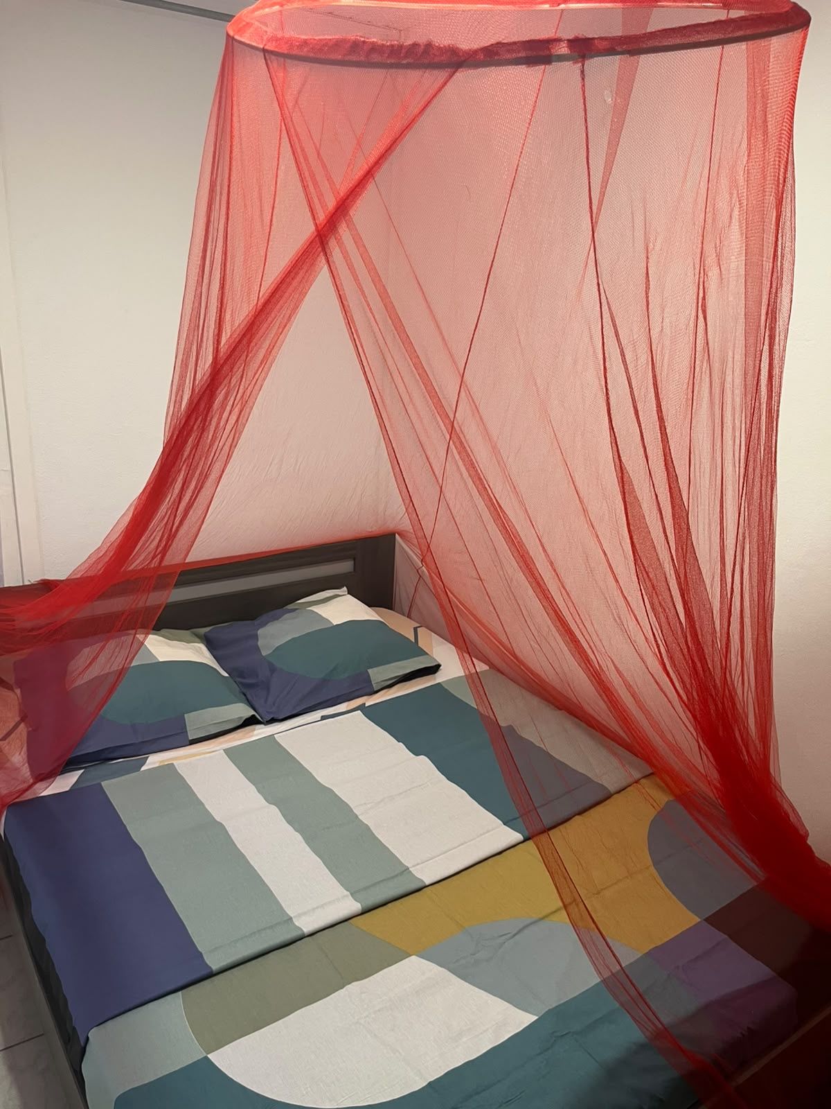 Un lit avec une couvre-lit colorée et une moustiquaire rouge.