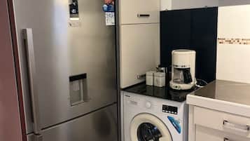 Eine kleine Küche mit einem Edelstahlkühlschrank, einer Waschmaschine und einer Kaffeemaschine.