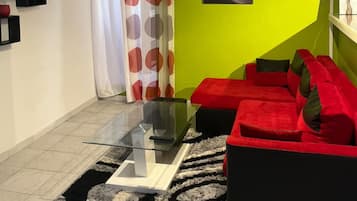 Una sala de estar moderna con una mesa de centro de vidrio, un sofá rojo y un televisor de pantalla plana montado en la pared.