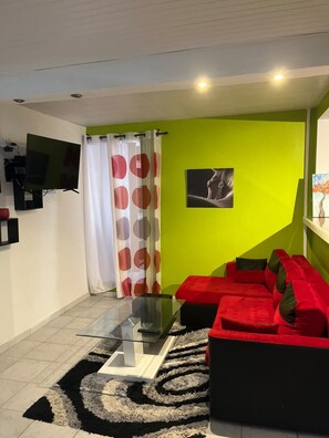 Una sala de estar moderna con una mesa de centro de vidrio, un sofá rojo y un televisor de pantalla plana montado en la pared.