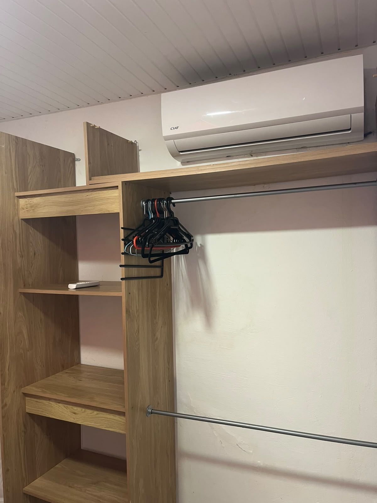 Una habitación con un armario de madera, una pared blanca y un equipo de aire acondicionado instalado en el techo.