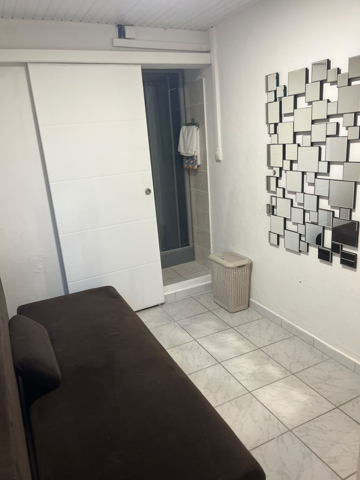 A room with a brown sofa, a white door, a wall-mounted mirror, and a small basket.